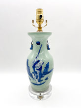 Load image into Gallery viewer, Celadon glazed ceramic figural vase lamp featuring a hand-painted blue scene of a child beneath a round moon, accented with small side handles, mounted on a clear acrylic base with a polished brass socket.