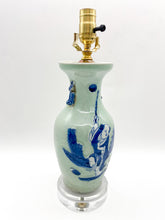 Load image into Gallery viewer, Celadon glazed ceramic figural vase lamp featuring a hand-painted blue scene of a child beneath a round moon, accented with small side handles, mounted on a clear acrylic base with a polished brass socket.