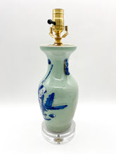 Load image into Gallery viewer, Celadon glazed ceramic figural vase lamp featuring a hand-painted blue scene of a child beneath a round moon, accented with small side handles, mounted on a clear acrylic base with a polished brass socket.
